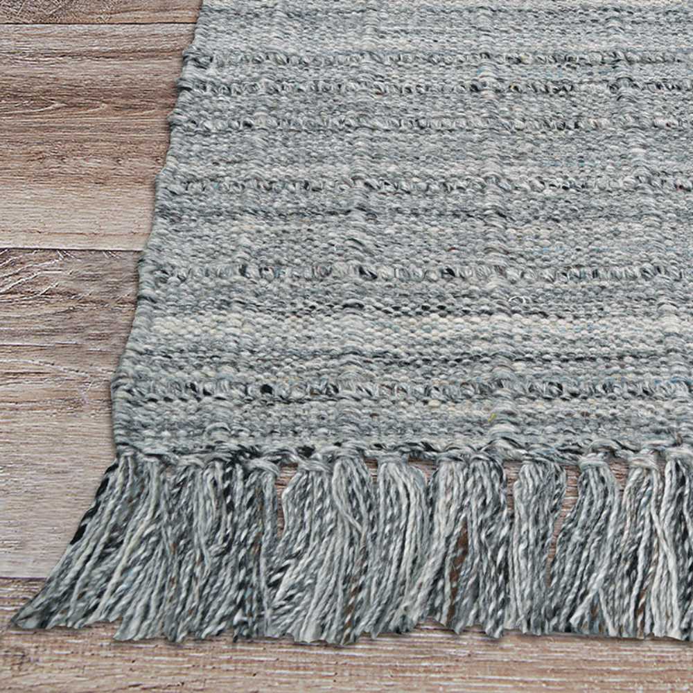 The edge of the Couristan Ascot Indoor/Outdoor Rug - Windowpane/Tweed features thick fringe and a chunky, handmade look on a light wood floor