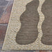 The edge of the Couristan Castille Indoor/Outdoor Rug - Fiore/Mocha rests neatly on a stone surface