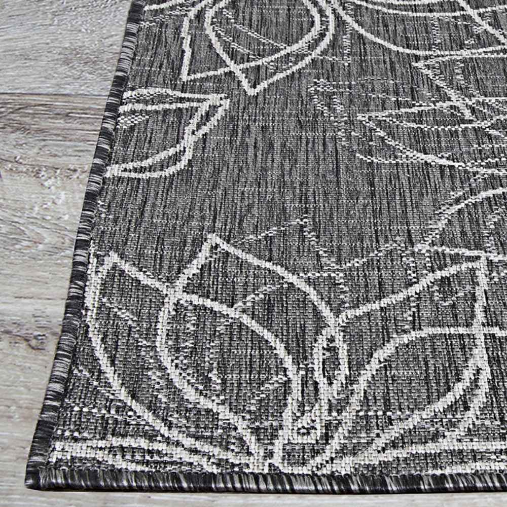 The edge of the Couristan Charm Indoor/Outdoor Rug - Botanical/Ash rests on wood flooring