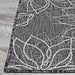 The edge of the Couristan Charm Indoor/Outdoor Rug - Botanical/Ash rests on wood flooring