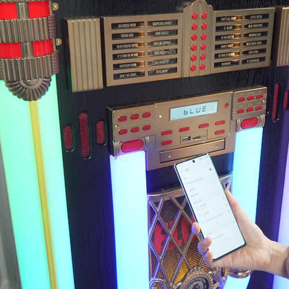 The image highlights the Bluetooth functionality of Arkrocket x Elvis Presley Saturn V Full Size Bluetooth Vinyl Record Jukebox with a smartphone being used to connect wirelessly