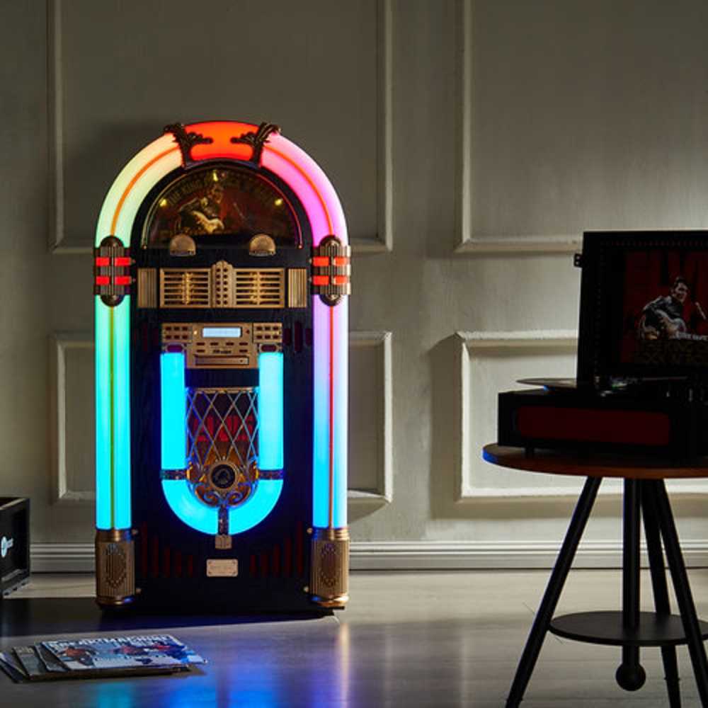 The image shows Arkrocket x Elvis Presley Saturn V Full Size Jukebox with Stand in a home setting glowing brightly with multi-colored lights