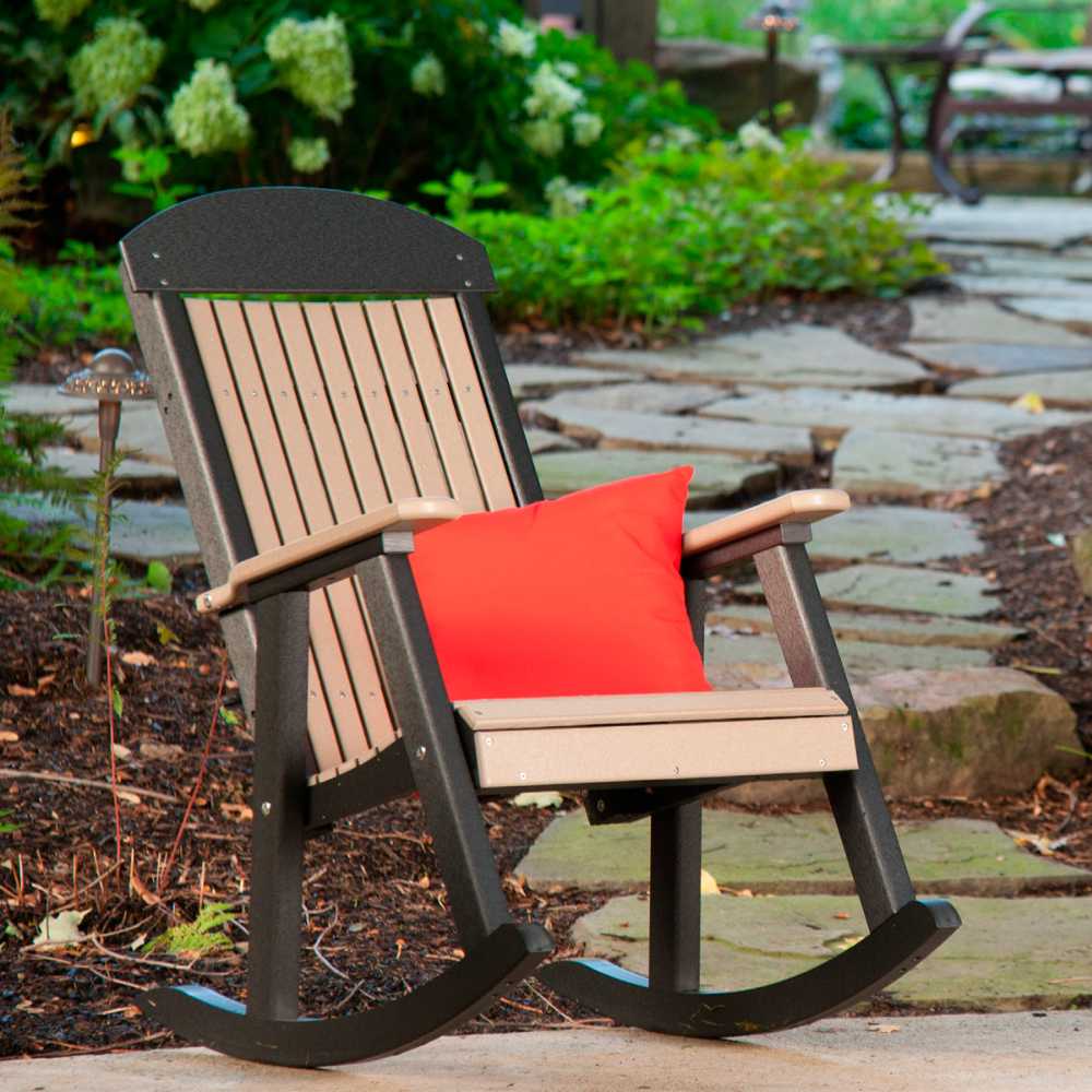 The image shows a cedar and black LuxCraft Porch Rocker in a garden setting with by a vibrant red cushion placed on the seat