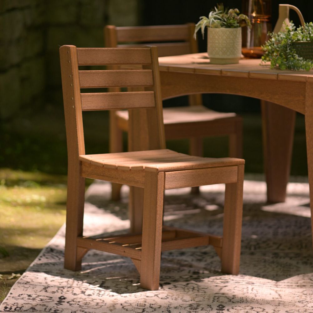 The image shows a sturdy wooden chair with a slatted back and seat, part of the LuxCraft Celeste Furniture Set, placed outdoors near a table on a patterned rug