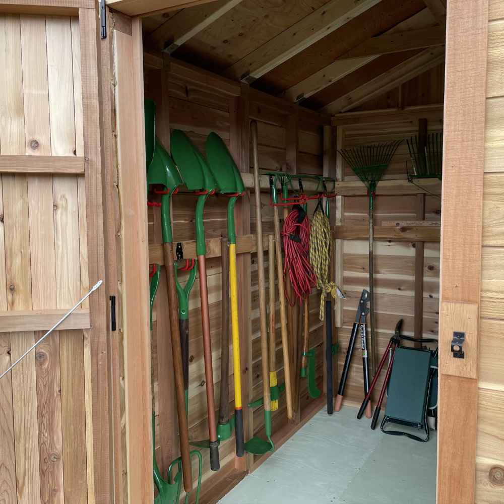 The interior view of a shed with garden shovels, rakes, and tools hanging neatly on the wall inside the Outdoor Living Today 8×8 Gardener Shed