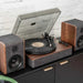 The needle is lowered onto a spinning vinyl on the Crosley Nocturne Record Player With Speakers - Charcoal, with two matching speakers on a dark sideboard