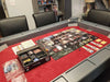 This Game Theory Tables Origins Lit Game Table is set up with a detailed board game on a red-felt surface, surrounded by cup holders and ample space for game pieces and cards