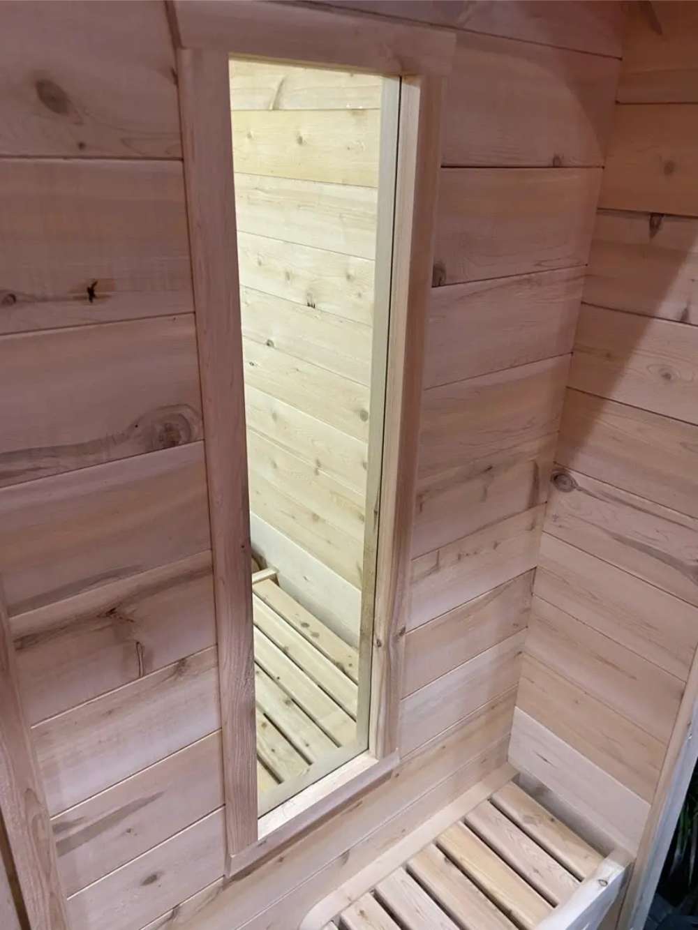 This image features a tall, narrow window beside a corner bench inside Sawmill Structures Box Sauna