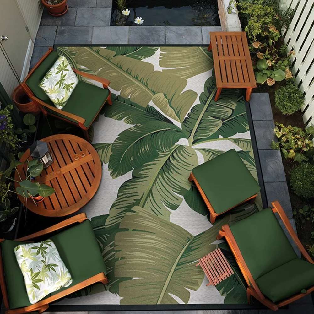 Top-down view of Couristan Dolce Indoor/Outdoor Rug - Palm Lily/Hunter Green-Ivory in a garden patio setting surrounded by wooden furniture and greenery