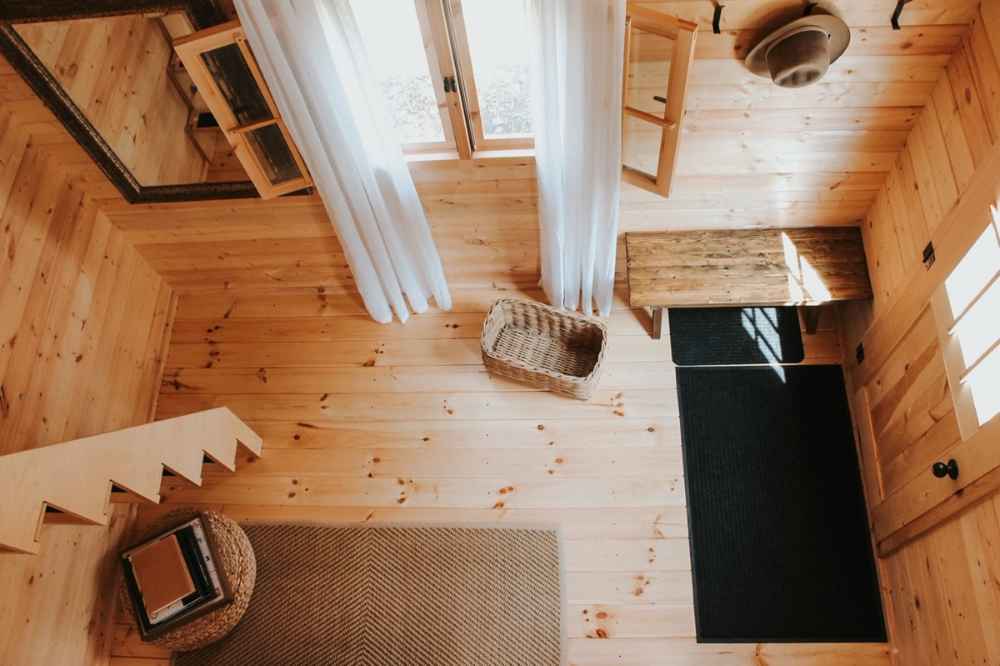 Top-down view of the Sawmill Structures BlueWater Loft 160 38mm Garden Room entryway shows a rustic wood floor, a woven basket, bench, and natural sunlight coming through sheer curtains