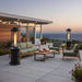 Two Outdoor Order Axis Collapsible Heater units glow at either end of a green-cushioned patio lounge set with an ocean view at dusk