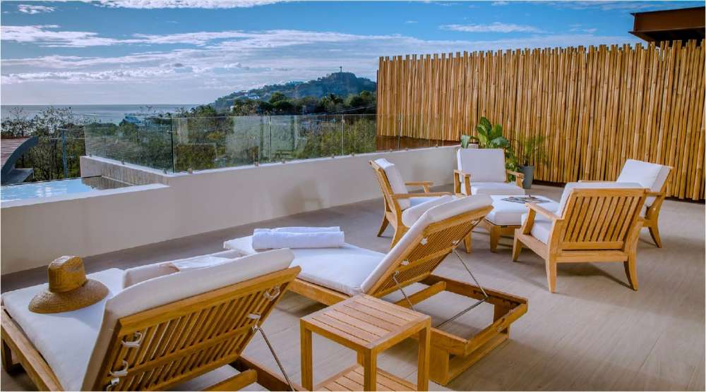 Two Westminster Teak Horizon Chaise Lounger chairs with white cushions rest on a scenic patio overlooking the ocean