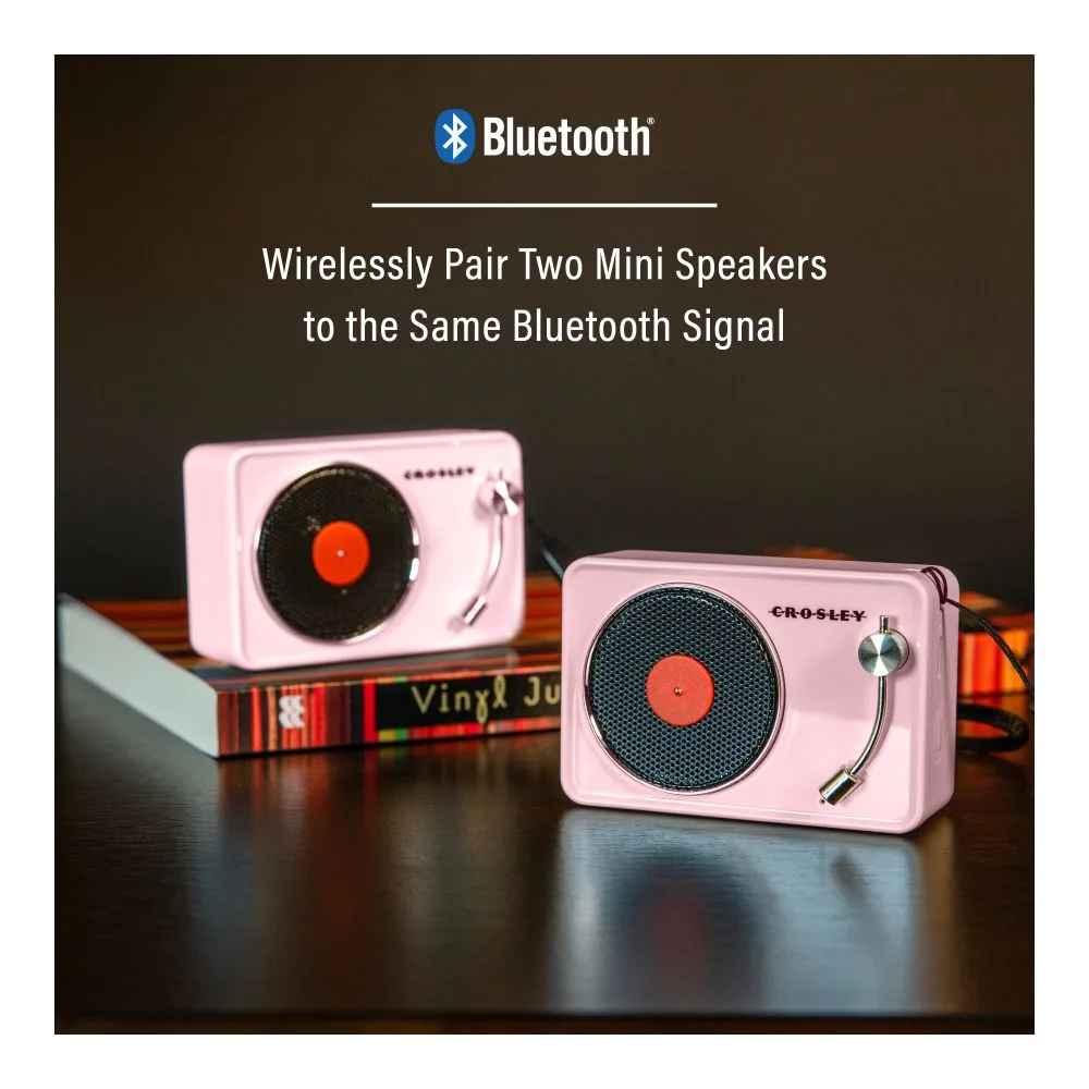 Two Crosley Mini Turntable Bluetooth Speakers - Pink are paired wirelessly via Bluetooth, displayed on a tabletop with books