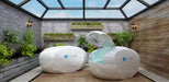 Two Dreampod Home Float Plus units are placed together in a greenhouse-style room with greenery on the walls, one open to show a soothing blue interior