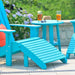 Two LuxCraft Deluxe Adirondack Footrests in bright turquoise are placed outdoors next to matching Adirondack chairs and a round table with glasses of iced tea