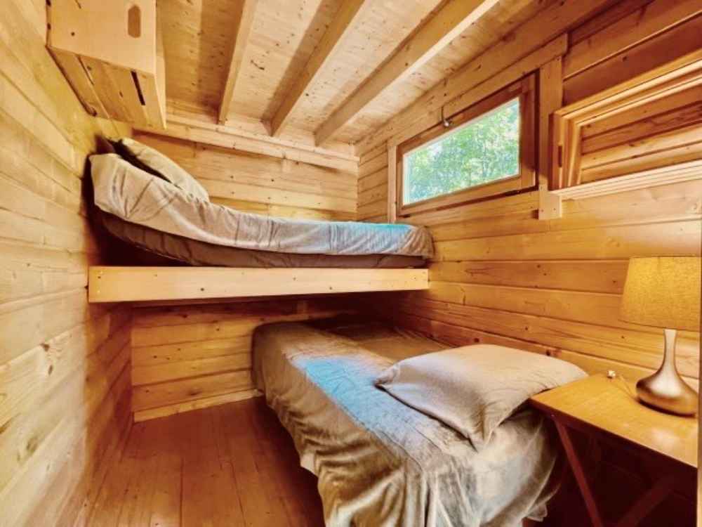 Two single beds, one lofted and one on the floor, fill a small wood-paneled room in the Sawmill Structures Edwin Lake House 70MM Garden Room