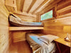 Two single beds, one lofted and one on the floor, fill a small wood-paneled room in the Sawmill Structures Edwin Lake House 70MM Garden Room