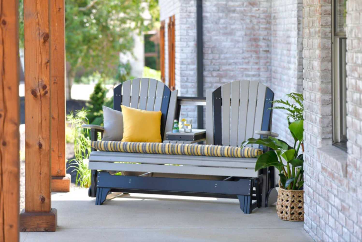 Two gray and black Adirondack-style glider chairs, each featuring a LuxCraft 15 Toss Pillow, are placed on a cozy porch