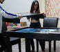 Two people assemble the Game Theory Tables The Meeples Champion Game Table by lifting its dining top, revealing a beautiful blue playing area underneath