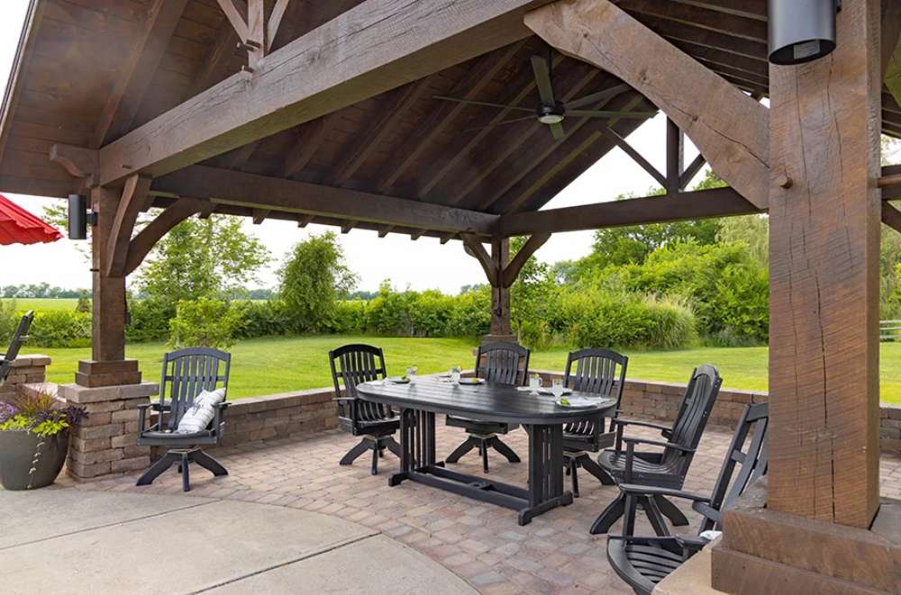 Underneath the Brookside Timber Frame Timber Retreat Pavilion, a spacious dining setup with black wooden chairs and a sturdy table