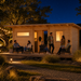 Urho 70 A wooden garden cabin illuminated at night with friends talking and laughing together on the deck.