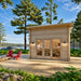 Front view of the Versa 107 70MM beside a lake in morning light, featuring broad glass panels, two exterior lamps, red chairs, and a pine forest.