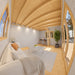 Bright Versa 160 Atrium Loft 70MM lounge with a white sofa, coffee table, workspace, potted tree, wooden loft ladder, and curved ceiling beams.