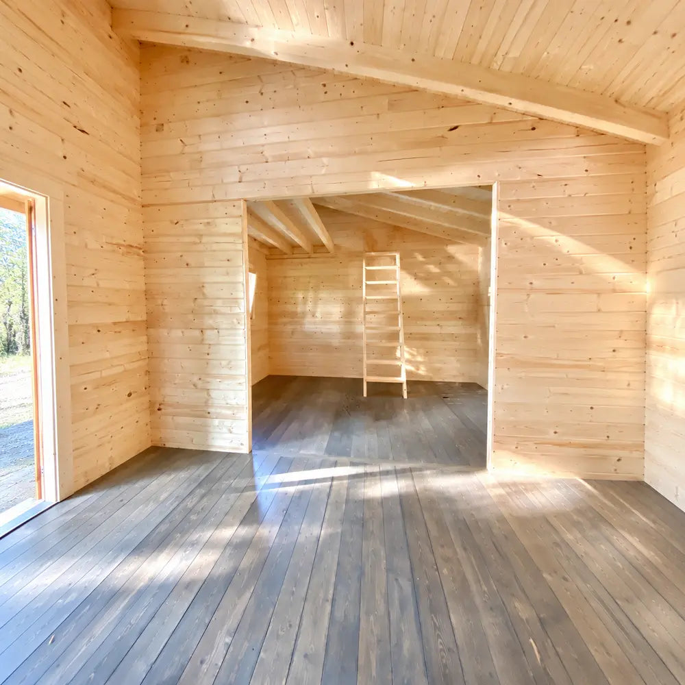 Empty sunlit Versa 240 70MM interior with natural timber walls, dark wood flooring, exposed beams, a wide opening to an adjoining room, and a wooden ladder.
