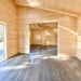 Empty sunlit Versa 240 70MM interior with natural timber walls, dark wood flooring, exposed beams, a wide opening to an adjoining room, and a wooden ladder.