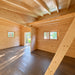 Unfinished Versa 240 70MM interior with exposed wooden roof beams, dark flooring, multiple windows, an open doorway, and a diagonal timber ladder.