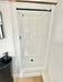 Walk-in shower in Sawmill Structures Wanderlove Tiny Home is white, compact, and framed by light shiplap walls with a black curtain rod