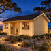 Wallis 44 Freedom Office illuminated at night on North Carolina’s Outer Banks, shown from the front-right angle among coastal dunes, sea oats and maritime trees, with people watching sports inside.