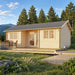 Wallis 44 wooden garden room with a dark gabled roof, glazed door and paired windows, set on a wooden deck with outdoor dining furniture amid trees and mountain scenery.