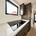 Sleek black glass cooktop built into a white marble-patterned counter beneath a large window in the Wanderlove Tiny Home kitchen.