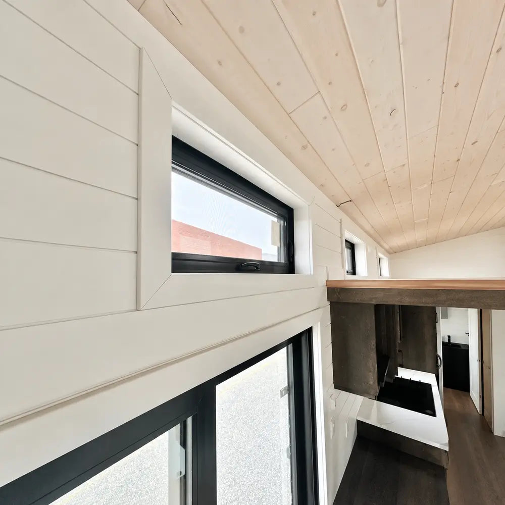 Slim black-framed clerestory windows set high above white shiplap walls and a loft railing inside the Wanderlove Tiny Home.