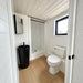 Compact Wanderlove Tiny Home bathroom with a white toilet, tall black sink, walk-in shower, window, and white shiplap walls.
