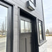 Exterior close-up of the Wanderlove Tiny Home’s black front door framed by dark siding, narrow windows, and a rectangular wall light.