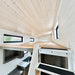 Low-ceiling loft inside the Wanderlove Tiny Home with white shiplap walls, light wood surfaces, several windows, and compact staircase access.