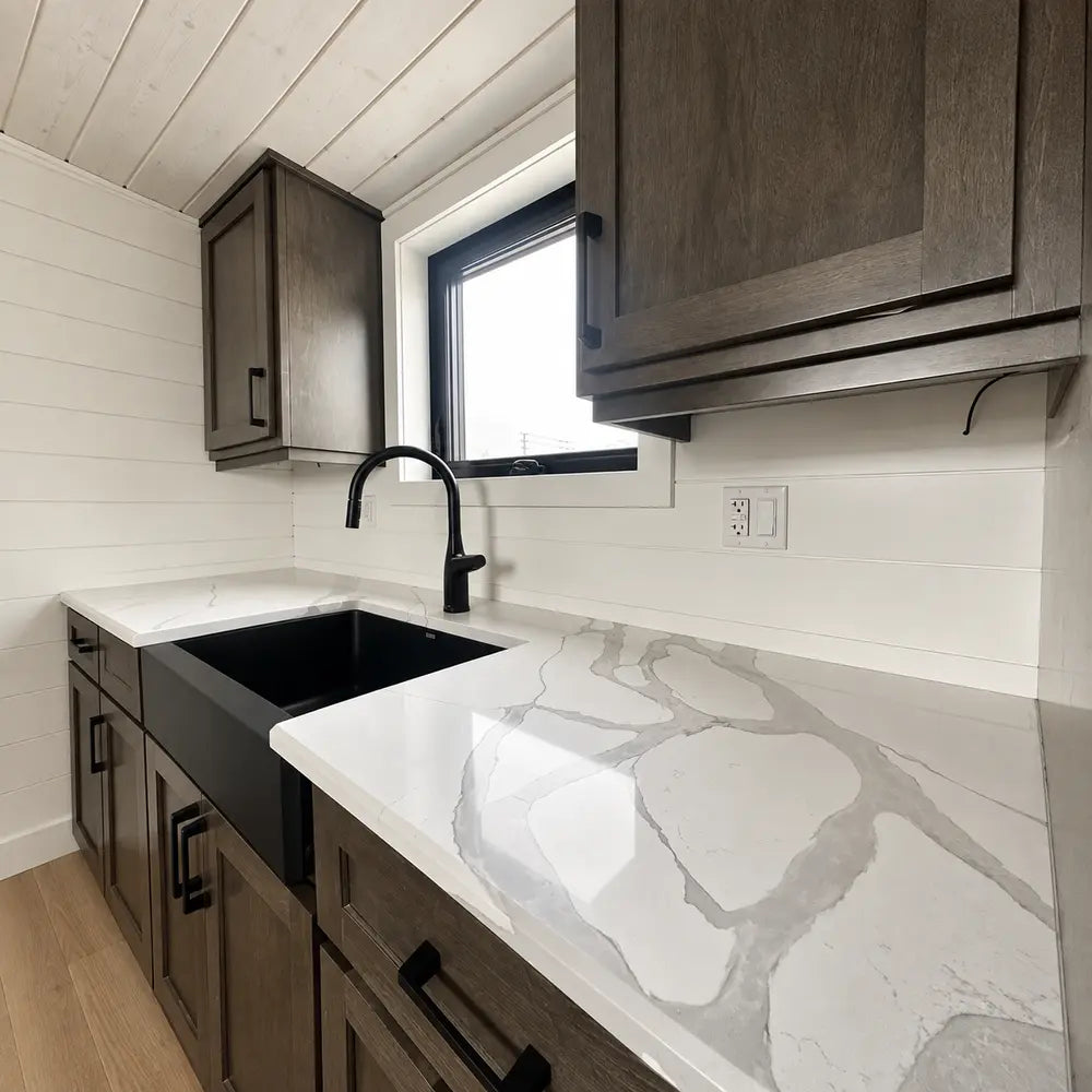 Wanderlove Tiny Home kitchen close-up with a marbled white countertop, deep black sink and faucet, and rustic dark wood cabinetry.