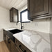 Wanderlove Tiny Home kitchen close-up with a marbled white countertop, deep black sink and faucet, and rustic dark wood cabinetry.