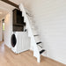 Compact white staircase with dark step grips rising above a washer-dryer inside the bright Wanderlove Tiny Home.