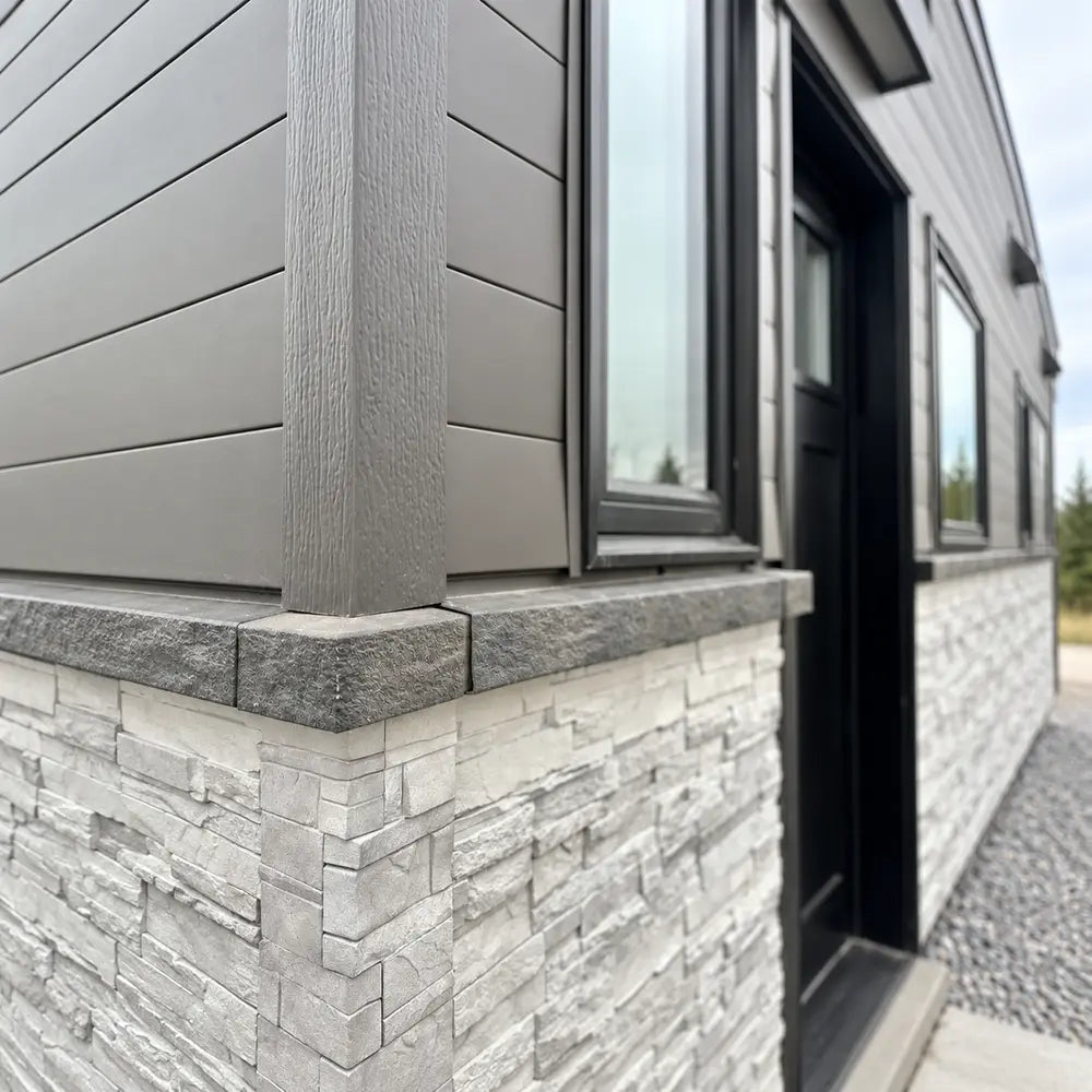 Close corner view of the Wanderlove Tiny Home showing textured faux-stone siding beneath dark horizontal cladding and black-trimmed windows.