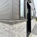 Close corner view of the Wanderlove Tiny Home showing textured faux-stone siding beneath dark horizontal cladding and black-trimmed windows.