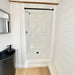 Compact white walk-in shower in the Wanderlove Tiny Home framed by light shiplap walls and a black curtain rod.