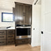 Stainless steel wall oven built into dark wood cabinetry beside a white sliding door inside the Wanderlove Tiny Home.