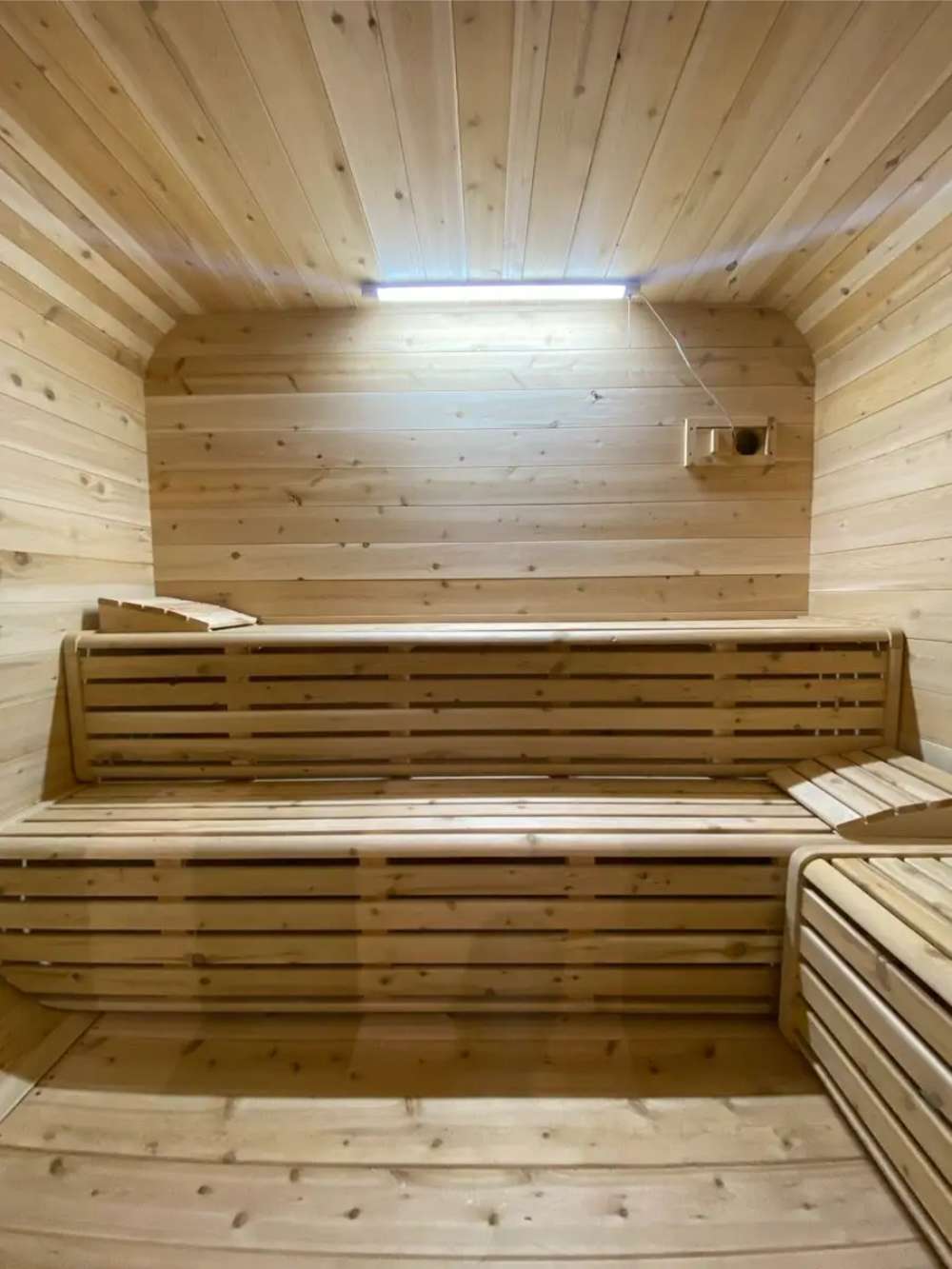 Warm interior of Sawmill Structures Box Sauna with smooth wood walls and two-tier bench seating under a bright overhead light