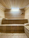 Warm interior of Sawmill Structures Box Sauna with smooth wood walls and two-tier bench seating under a bright overhead light
