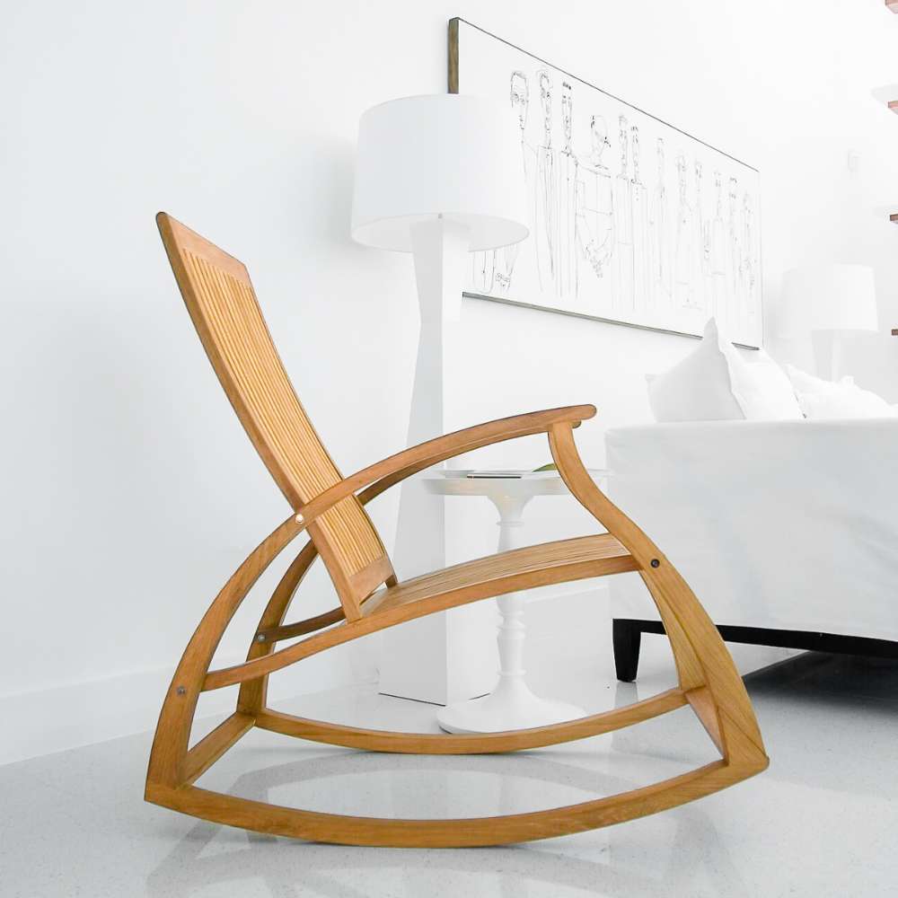 Westminster Teak Aria Rocker appears in a modern room next to a white table and couch, showing how it fits into a home setting