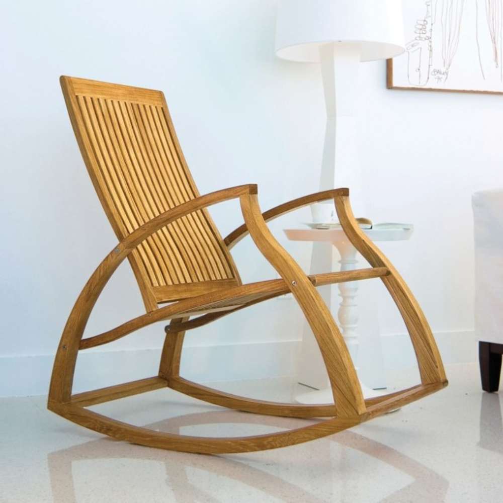 Westminster Teak Aria Rocker sits on a glossy floor beside a small white table and lamp