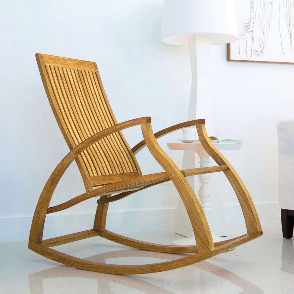 Westminster Teak Aria Teak Rocker sits in a bright indoor space beside a small white table and lamp
